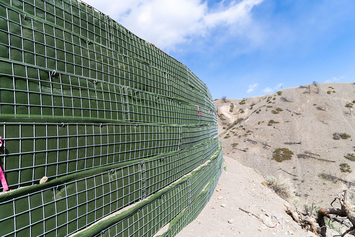 The MSE wall is built with stacked, fabric-lined wire mesh structural supports to reinforce the corner of the roadway.